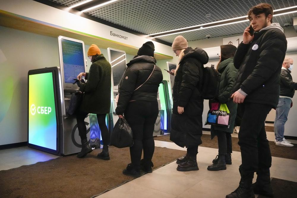 FILE - People stand in line to withdraw money from an ATM in Sberbank in St. Petersburg, Russia, Friday, Feb. 25, 2022. In the days since the West imposed sanctions on Russia over its invasion of Ukraine, ordinary Russians are feeling the painful effects — from payment systems that won't operate and problems withdrawing cash to not being able to purchase certain items. (AP Photo/Dmitri Lovetsky, File)